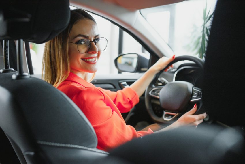 Femeie zâmbitoare la volanul unui autoturism, imagine ilustrativă pentru serviciile de închirieri auto la Aeroportul Iași.